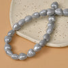 A string of heart-shaped gray ceramic beads laid on a light beige surface.