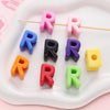 A collection of colorful acrylic letter beads shaped like the letter R in various shades and sizes arranged on a white tray.