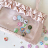 A pink fabric pouch filled with a collection of colorful mini pin badges and a ruffled edge.