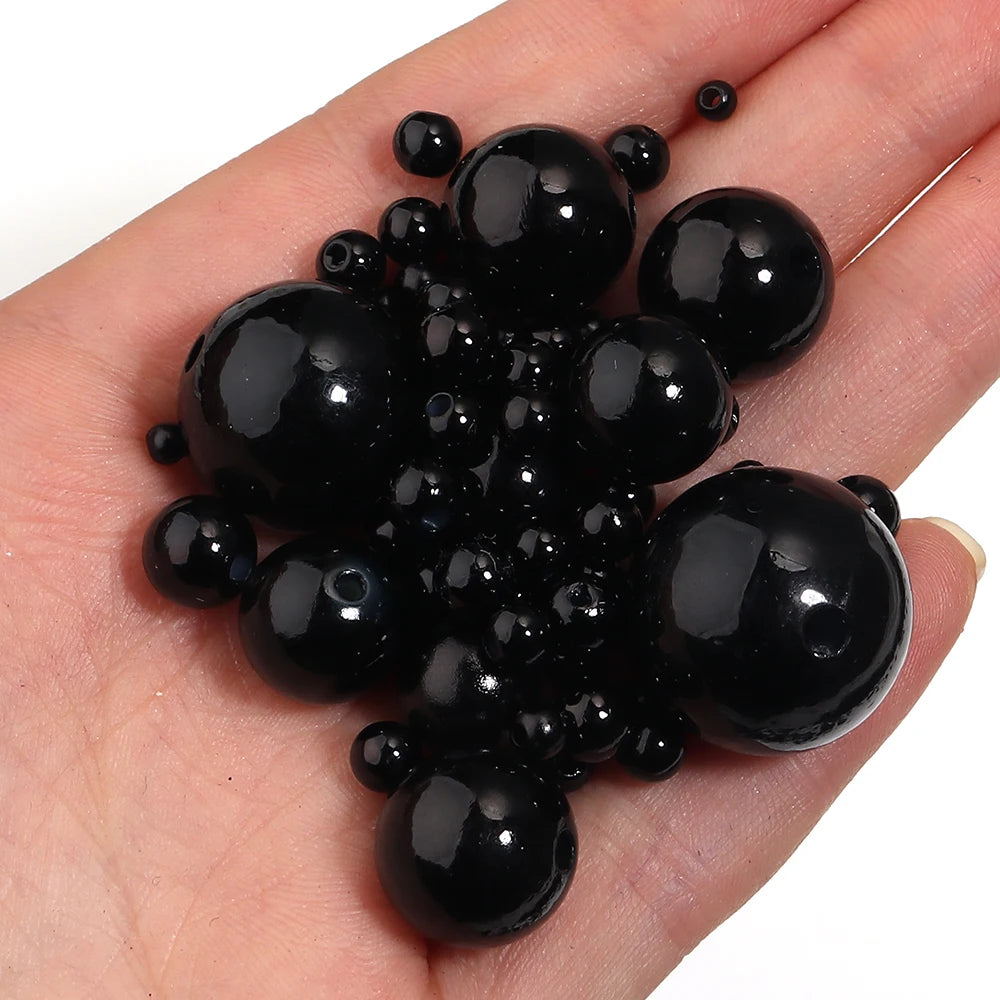 A cluster of small, round black imitation pearl beads is held in a person's hand.