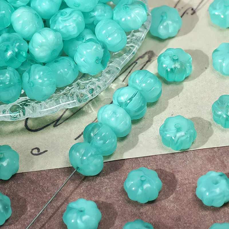 A collection of light blue translucent pumpkin-shaped resin beads for jewelry making displayed on a clear dish.
