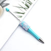 A close-up of a turquoise ballpoint pen with a sparkly blue sequin tip resting on white paper.