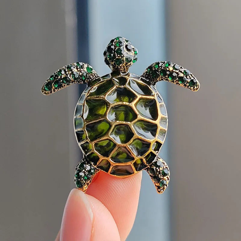A detailed gemstone turtle brooch pin featuring green and gold iridescent stones.