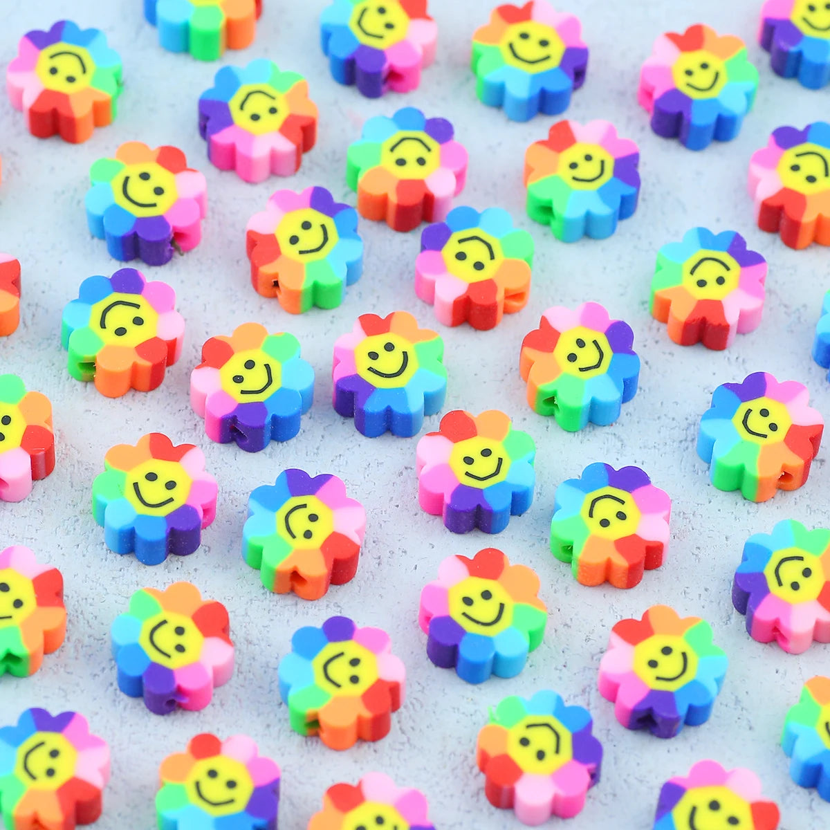 A collection of colorful polymer clay smiling sunflower beads scattered on a white surface.