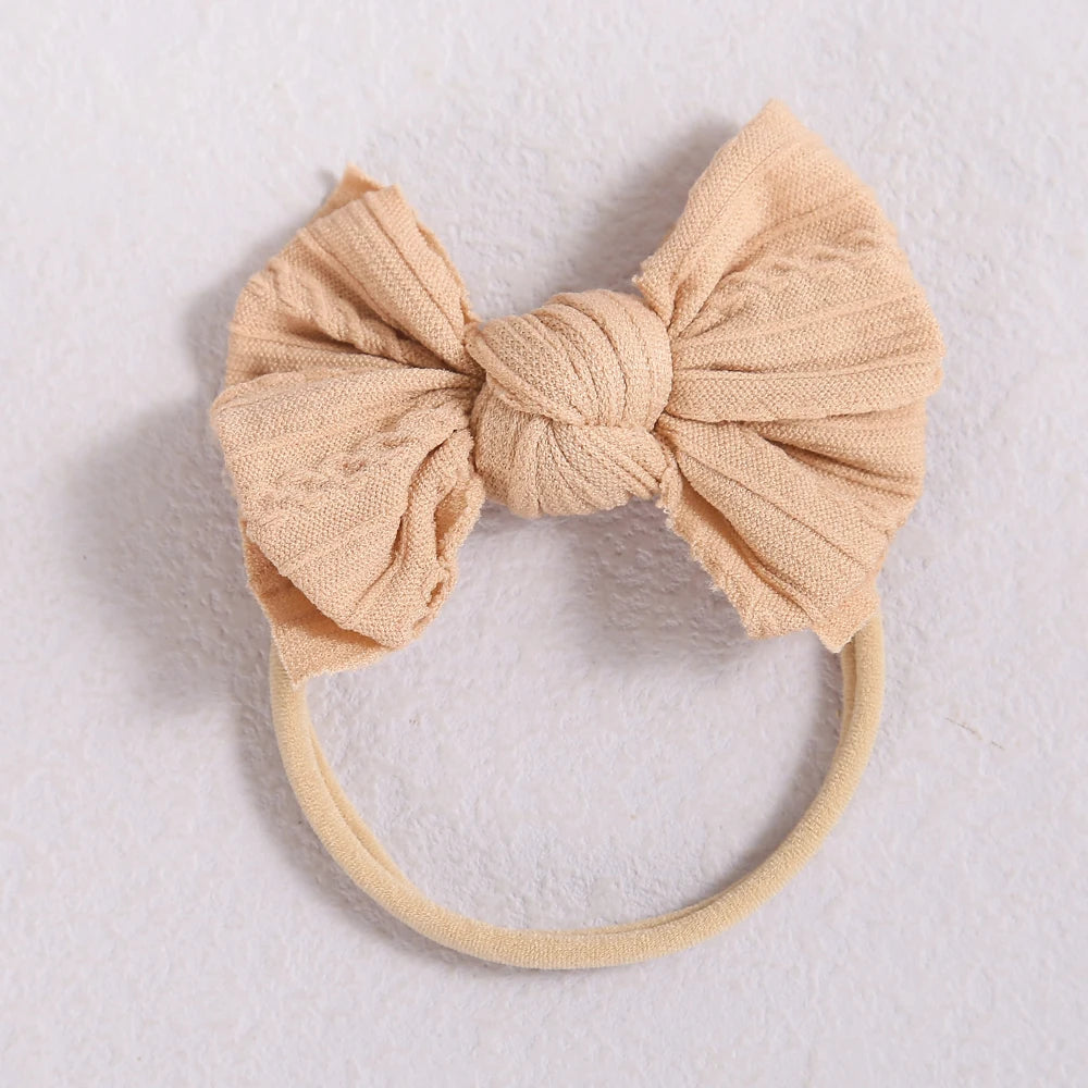 A beige fabric bow headband with a soft elastic band, suitable for a baby or girl.