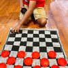 A child is playing a game on a black and white checkered rug with red pieces.