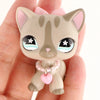A small, light brown cat figure with pink accents and a beaded collar is held in a person's hand.