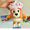 An orange and white plush toy resembling a dog wearing a white chef's hat.