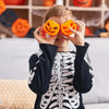 A young child is squeezing orange pumpkin and skeleton sensory toys over their eyes.