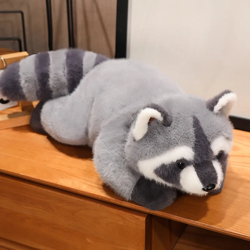 A gray and white raccoon plush toy resting on a wooden surface.