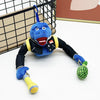 Juguete de dinosaurio de peluche azul con acentos amarillos y una fruta verde, junto a una jaula de alambre negra.
