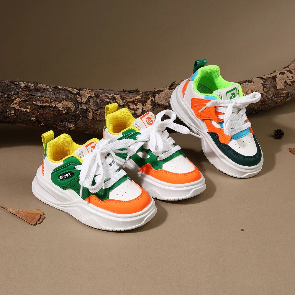 A pair of bright green, orange, and white casual sneakers with hook-and-loop straps resting on a brown surface next to a log.