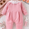 A pink quilted baby girl romper with a white lace collar lying on a white textured surface.