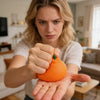 A woman holds a realistic orange stress ball in her hand, demonstrating the slow rising squeeze toy.
