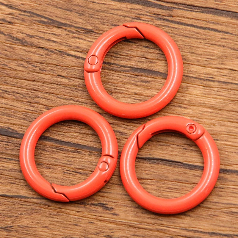 A set of ten bright orange metal O-ring spring clasps arranged in a triangle on a wooden surface.