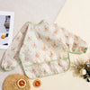 A light patterned waterproof long sleeve feeding bib lying on a beige surface with citrus slices.
