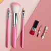 A collection of pink makeup brushes and applicators laid on a pink background.