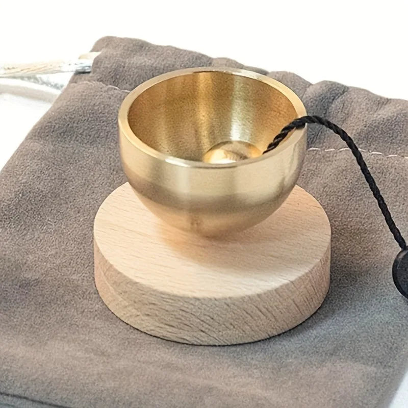 A brass singing bowl rests on a wooden base, tied with black cord, placed on a gray fabric.