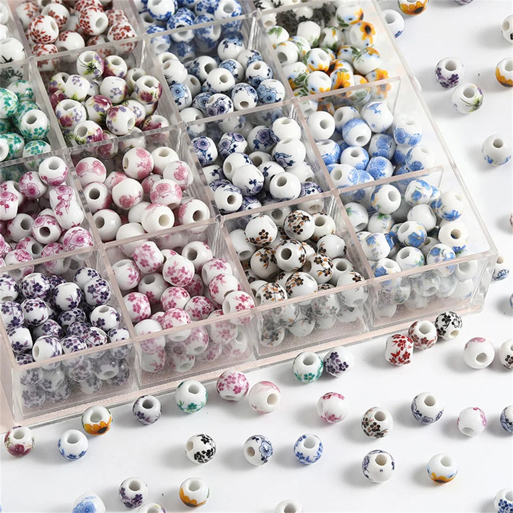 A clear plastic box filled with a variety of round ceramic flower beads in various colors and patterns for jewelry making