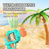 A turquoise water gun is shown in action, firing a stream of water toward a palm tree in a sunny outdoor setting.