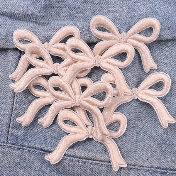 A set of light pink embroidered fabric bows on a denim garment.