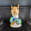 A plush toy resembling a dog or fox with orange fur and blue patterned ears sitting on a white base.