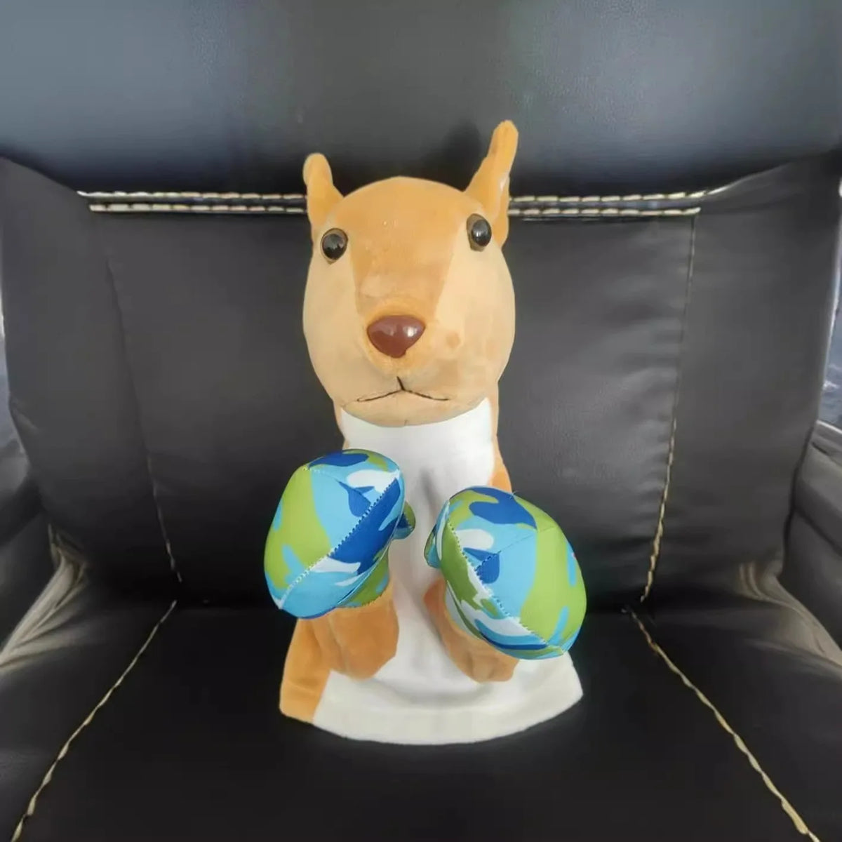 A plush toy resembling a dog or fox with orange fur and blue patterned ears sitting on a white base.