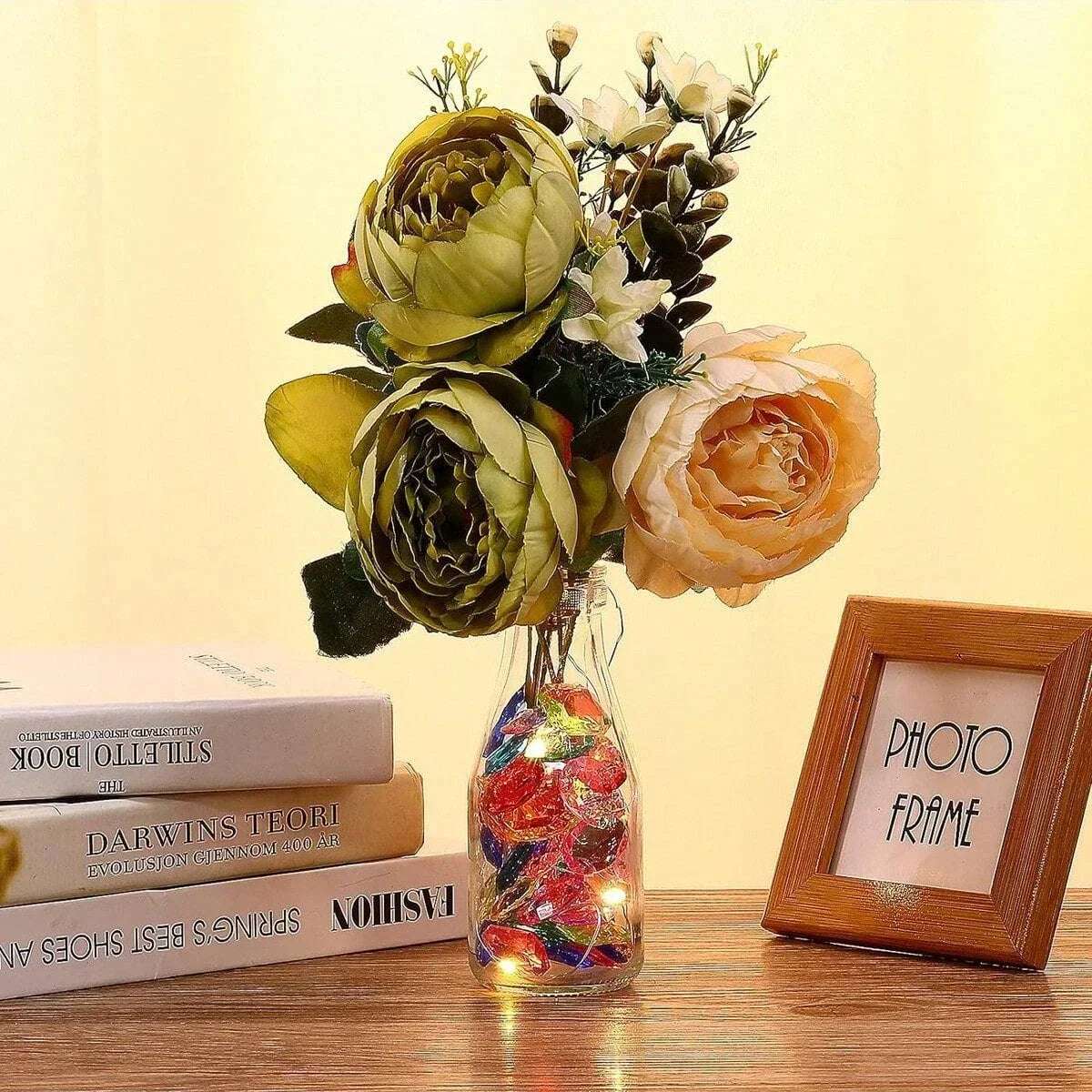 A bouquet of dried flowers and green foliage with a glass vase filled with sparkling red and orange acrylic gemstones.