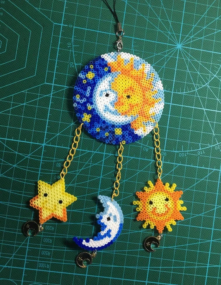 A hanging craft project made from colorful fuse beads shaped like a sun and moon on a green grid background.