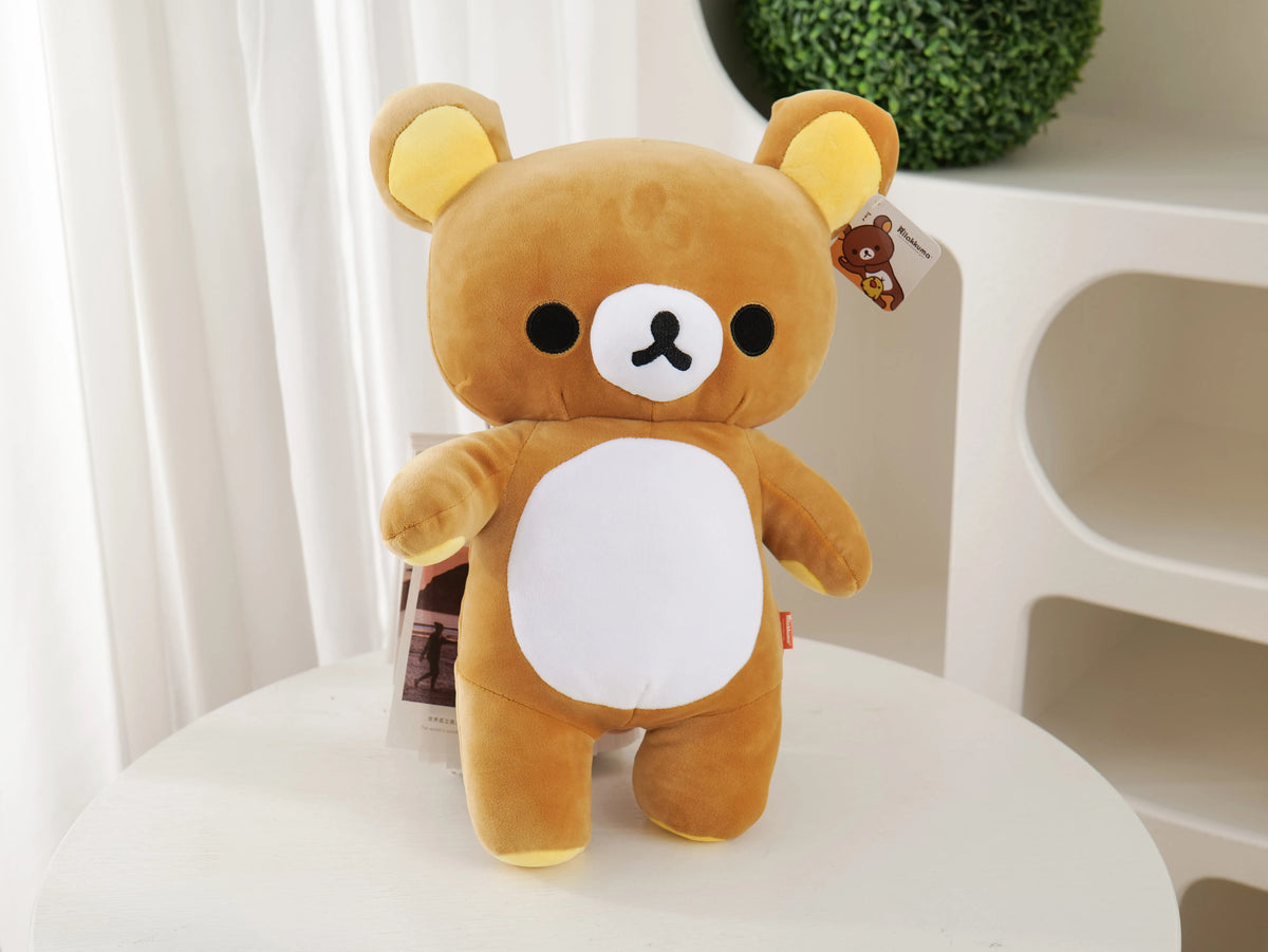 A fluffy brown Rilakkuma anime plush bear with a white chest patch sitting on a white surface.