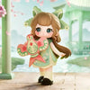 A collectible figurine of a girl with brown hair and green ears, holding a pink and green butterfly accessory in a serene out
