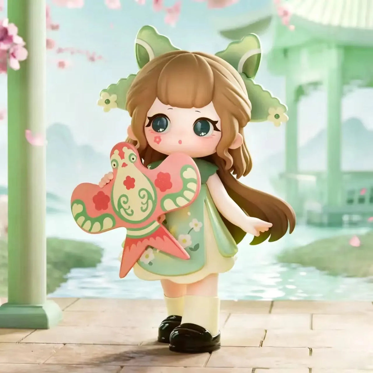 A collectible figurine of a girl with brown hair and green ears, holding a pink and green butterfly accessory in a serene out