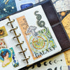 A close-up of a leather-bound journal featuring various retro astronomy and aesthetic stickers for planners and journals.