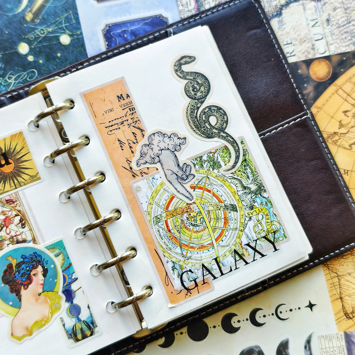 A close-up of a leather-bound journal featuring various retro astronomy and aesthetic stickers for planners and journals.