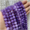 A hand holds a strand of purple gemstone beads, including amethyst and garnet varieties, for jewelry making.