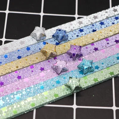 A collection of colorful glitter origami star paper strips arranged in horizontal rows on a black grid background.