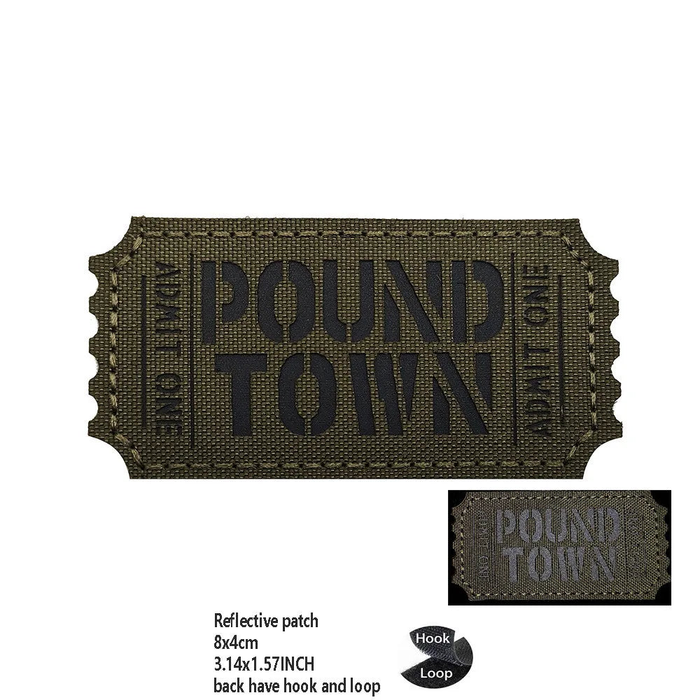 A dark olive green reflective patch with the text POUND TOWN embroidered on it.