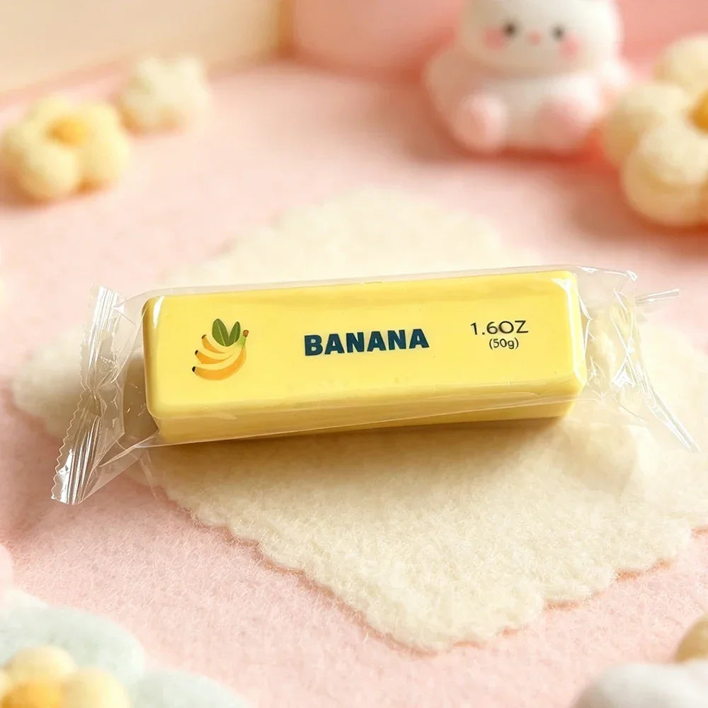 A yellow squishy fidget toy shaped like a banana is packaged in plastic on a pink surface.