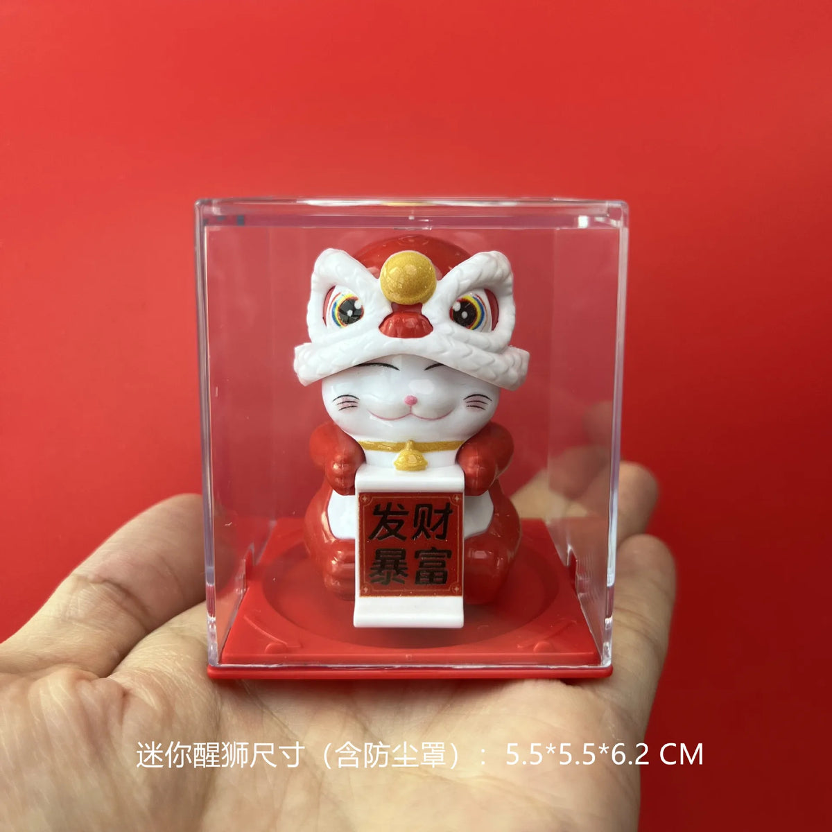 A white cat figurine with a red head wearing a crown is displayed inside a clear box on a red background.