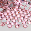 A close-up view of pink and silver glass crystal flatback rhinestones scattered on a white surface.