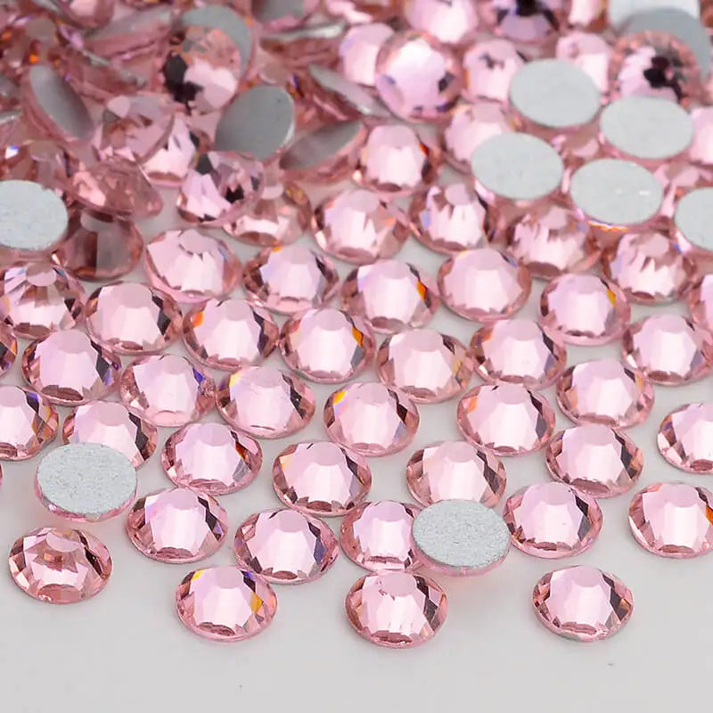 A close-up view of pink and silver glass crystal flatback rhinestones scattered on a white surface.