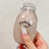 A hand holds a clear glass bottle filled with a milky liquid labeled Chiboki stress balls.