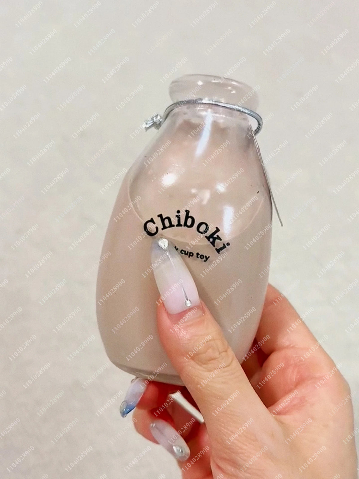 A hand holds a clear glass bottle filled with a milky liquid labeled Chiboki stress balls.
