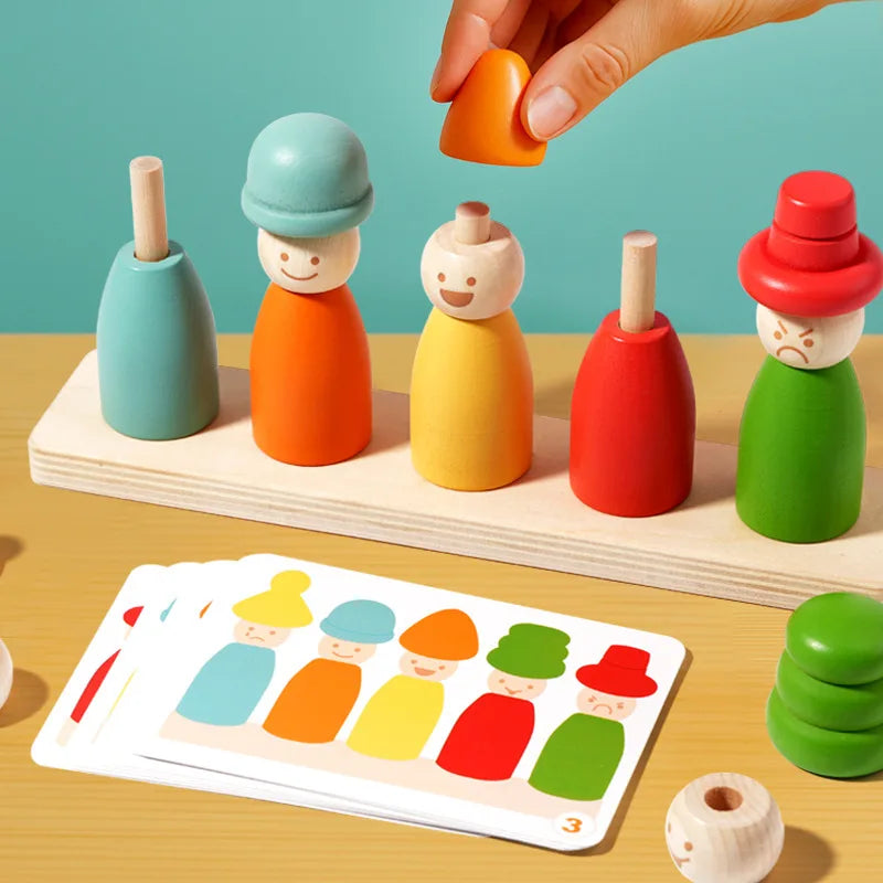 A hand is stacking wooden emotion figures of various colors on a light wooden board.