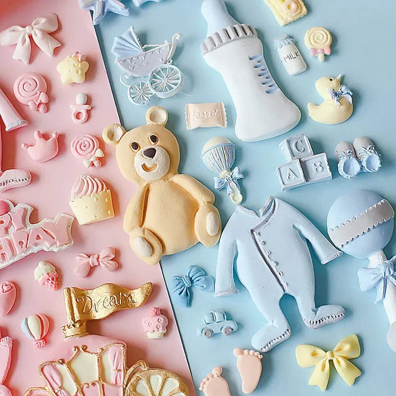 A collection of pink and yellow silicone baby-themed cake molds including a teddy bear, bottle, pacifier, and stroller.