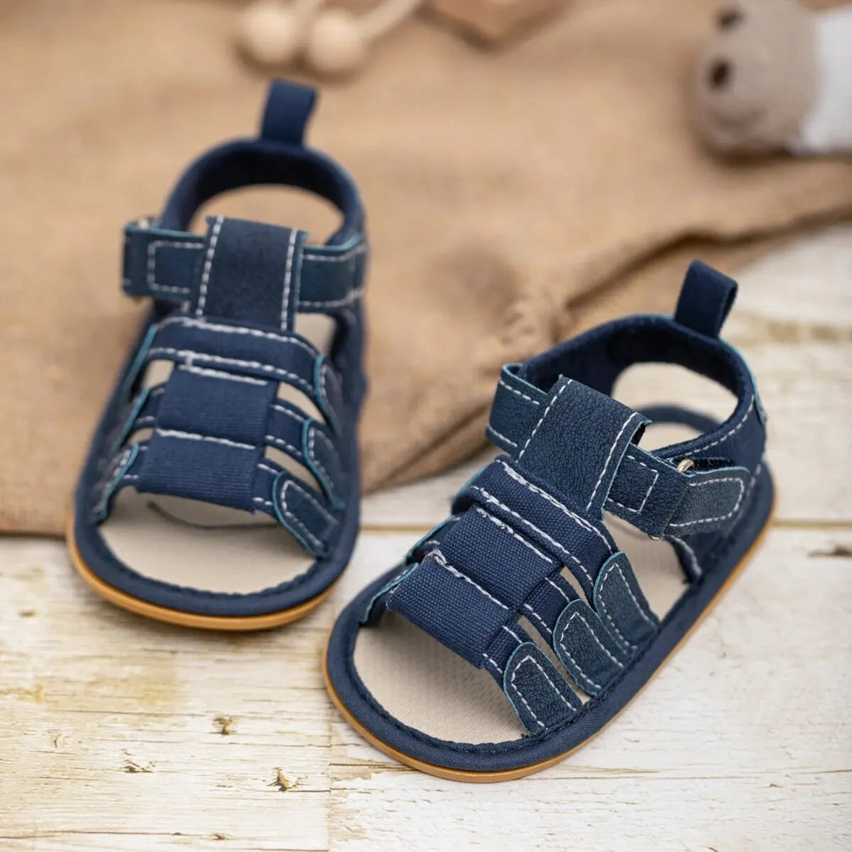 A pair of navy blue soft non-slip baby sandals for first walkers resting on a light wooden surface.
