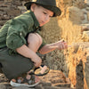 A young child is using a dinosaur excavation kit with tools to uncover fossils in an outdoor archaeological setting.