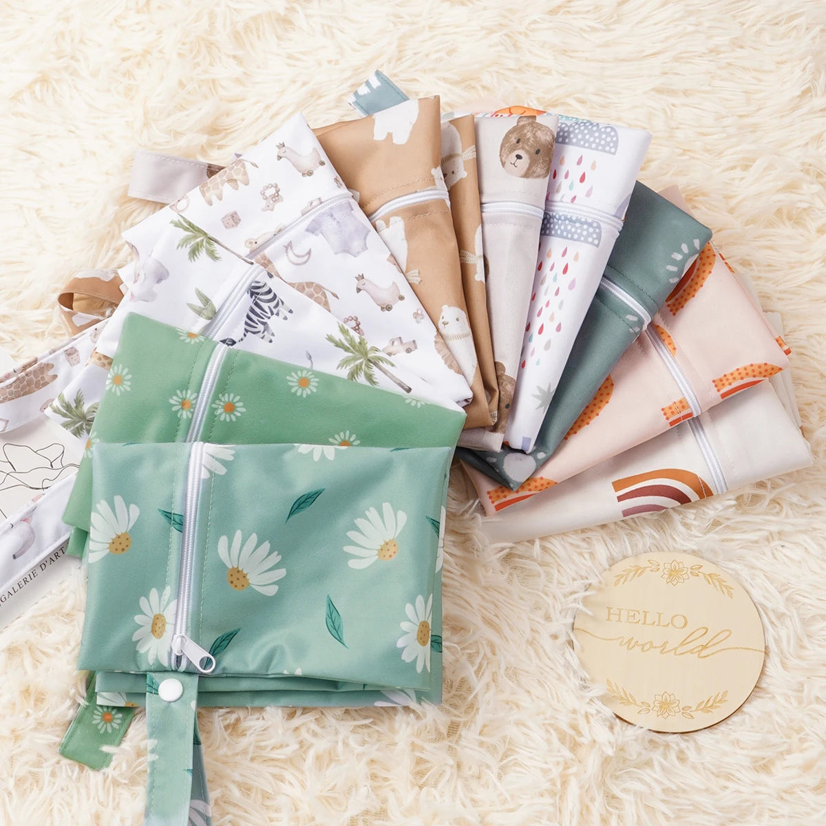 A collection of reusable waterproof baby wet bags in various neutral and pastel colors resting on a fluffy white surface.