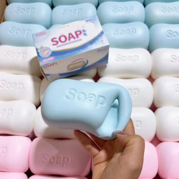 A hand holds a light blue stress relief squishy soap toy surrounded by other white and pink soap toys.