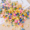 A close-up of mixed resin rhinestone pearls in various colors including pink, yellow, blue, and green scattered on a white ba